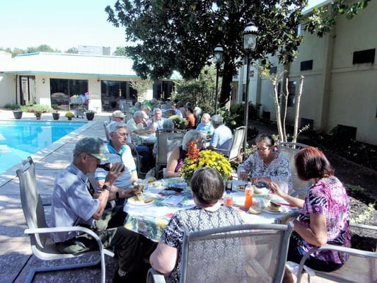 Group of seniors dining outdoors by a pool with flowers in the foreground