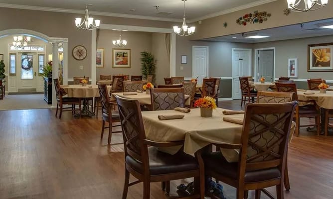 Dining room with tables and chairs, decorated with flowers and warm lighting.