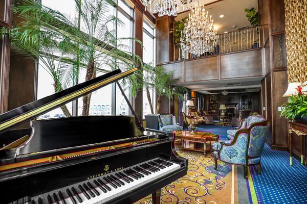 Grand piano in an elegant lounge with plants and chandeliers.