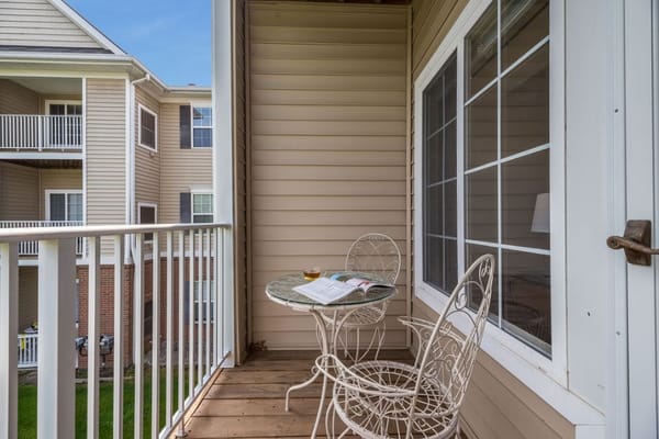 Small balcony with a table and chairs overlooking another building.