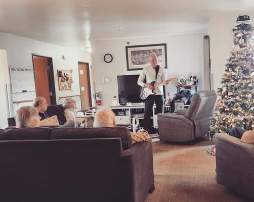 A musician performing with a guitar in a senior living common area during the holiday season.