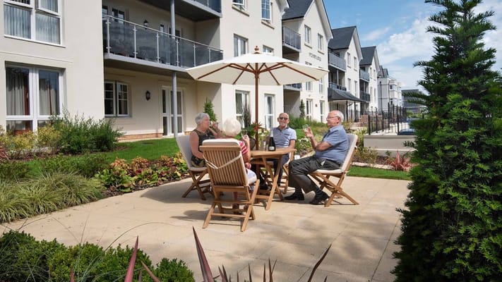 Group of four senior residents socializing under an umbrella outside Fitzford Lodge.