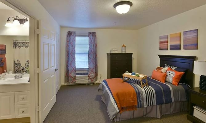 A well-decorated bedroom with an orange and blue theme, featuring a bed, decorative pillows, and a small table.