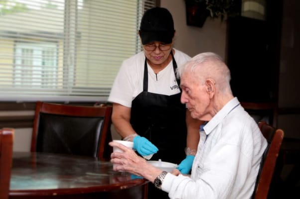 Staff assisting an elderly resident at a dining table