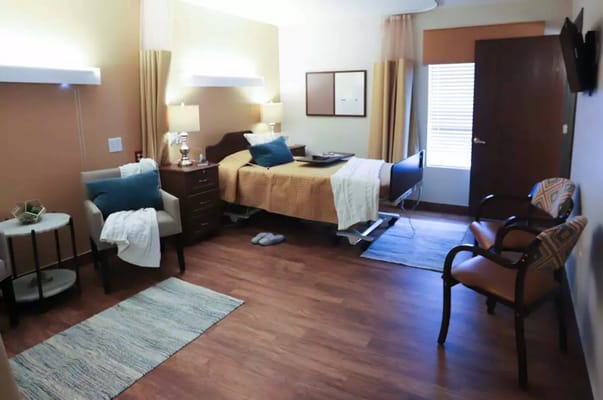 A cozy patient room featuring a bed, armchairs, and natural light.