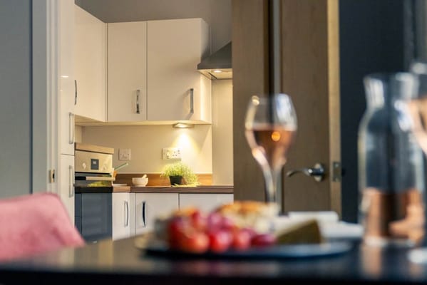 A modern kitchen with a dining table in the foreground and a glass of rosé wine.