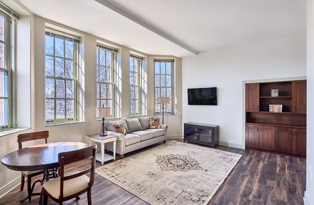 A cozy living room with large windows, a sofa, a coffee table, and a television.