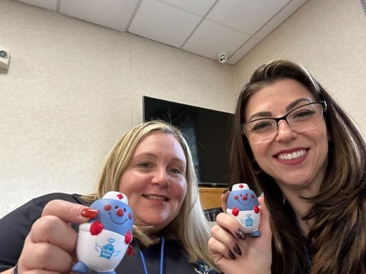 Two staff members smiling with mascot figures
