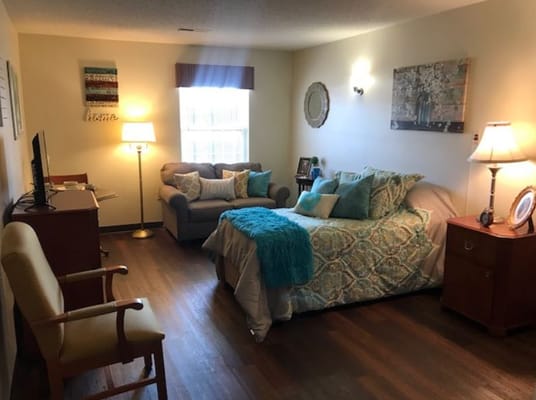 Cozy bedroom with a bed, couch, and lamp in a senior living facility