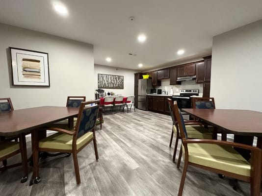 View of dining area with tables and kitchen in Lourdes Senior Community.