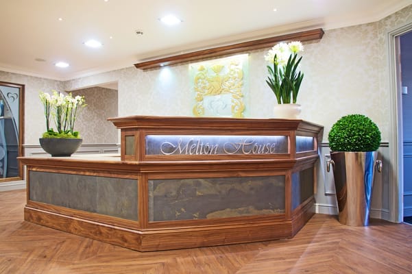 Wooden reception desk with floral arrangements at Melton House.