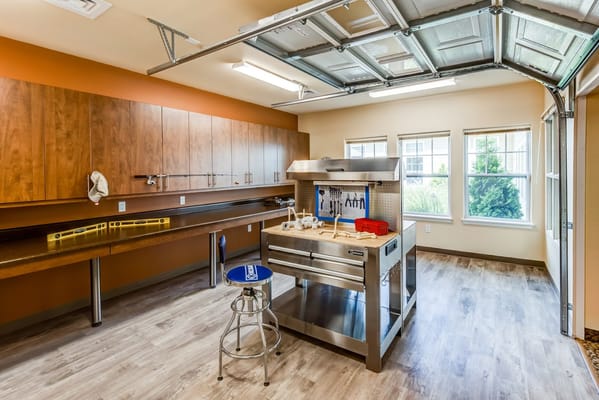 Bright workshop space with a stainless steel workbench and wooden cabinets.