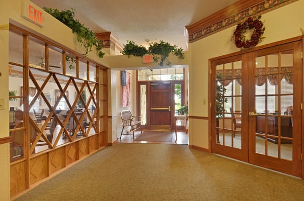 Interior hallway of Muncie Estates Senior Living featuring exit signs and decorative plants.