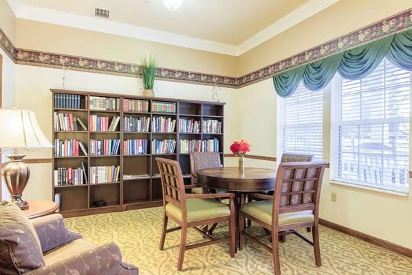 A cozy library with a wooden bookshelf filled with books and a round dining table.
