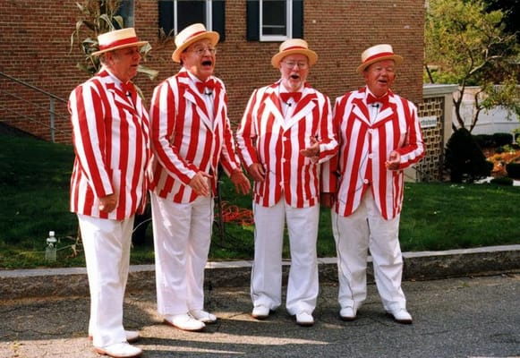 Four men in red and white striped jackets singing together