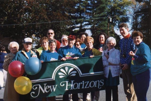 Residents and staff holding a New Horizons banner with balloons during a community event.