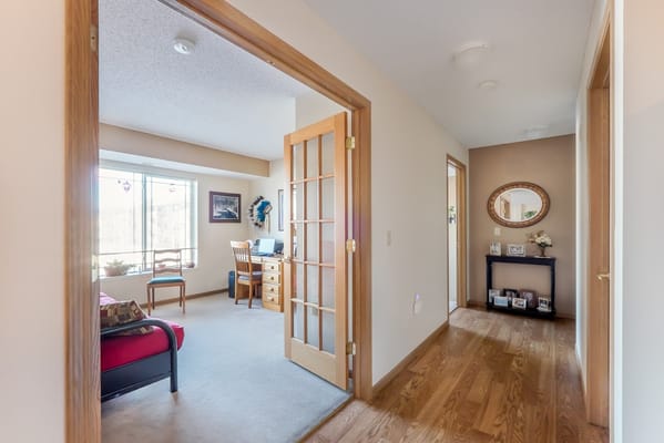 A hallway leading to a spacious living area with a desk and large windows.