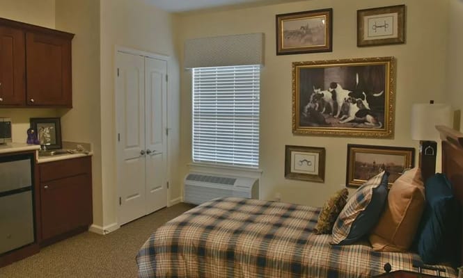 A bedroom featuring a plaid bedspread, artwork on the walls, and kitchenette.
