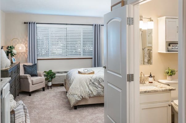 A well-decorated bedroom with an ensuite bathroom, featuring a comfortable bed and seating area.