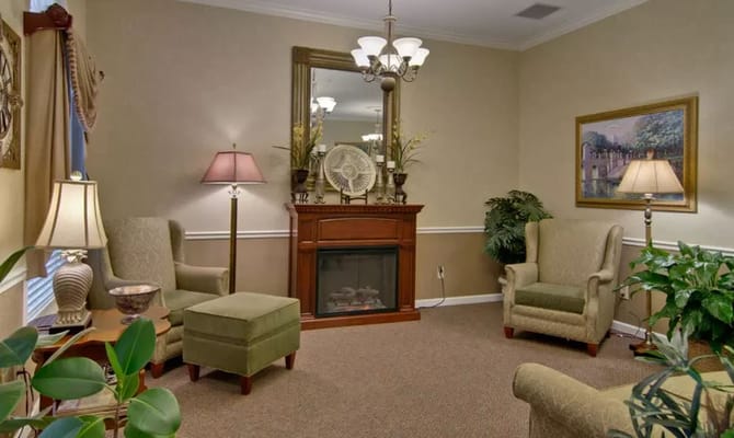 A comfortable living room with upholstered chairs, a fireplace, and decorative plants.