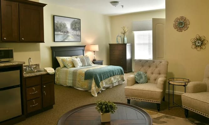 A well-furnished bedroom featuring a bed, seating area, and kitchenette.