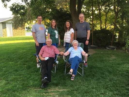 A family poses outdoors in a grassy area, sitting and standing in chairs.