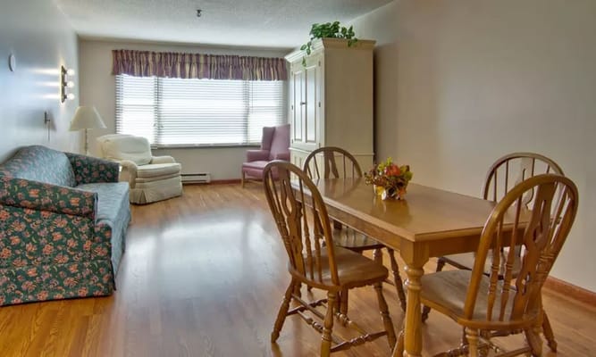 A living and dining area with a floral couch, wooden dining table, and bright window light.
