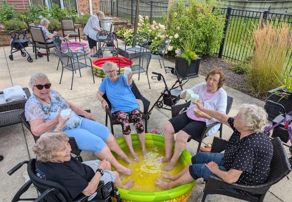 Group of seniors sitting around a kiddie pool, enjoying drinks and soaking their feet.
