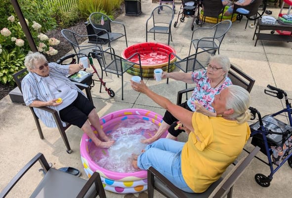 Three women sitting by a foot soaking pool, smiling and raising cups.