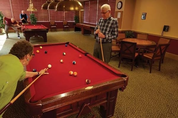 Two residents playing billiards in a community lounge