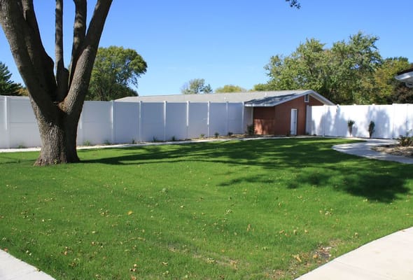 Well-maintained green lawn with a tree and white fence