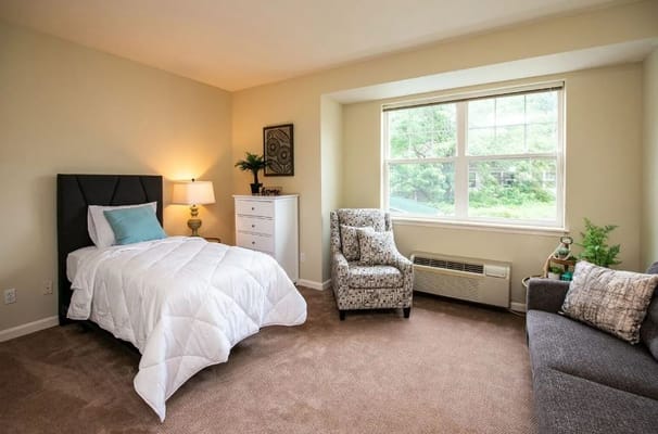 A cozy bedroom featuring a twin bed, armchair, and dresser.
