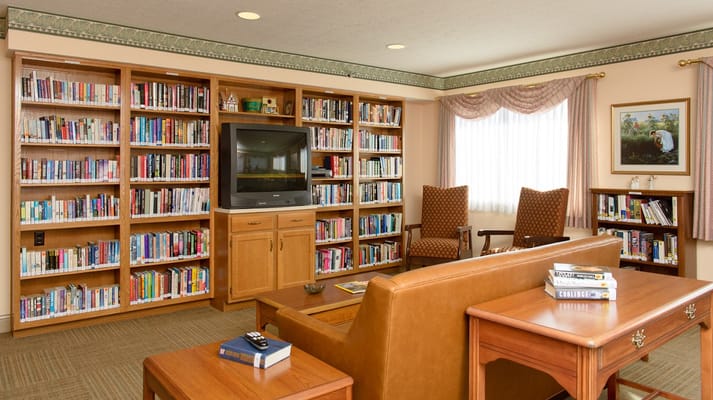 Interior view of a library with bookshelves, seating area, and television
