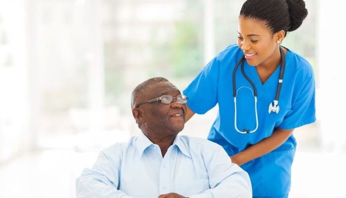 A nurse smiling while assisting a senior resident in a bright room.