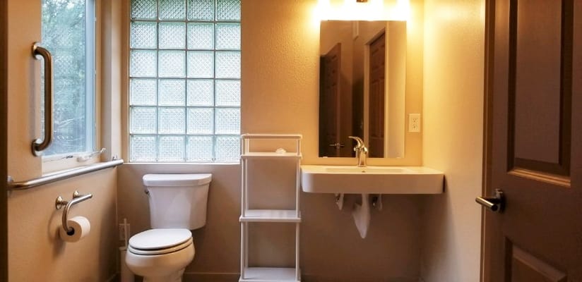 Bright bathroom with a toilet, sink, and glass block window.