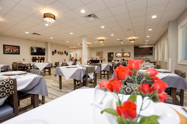 Spacious dining area with tables set for meals and flowers.