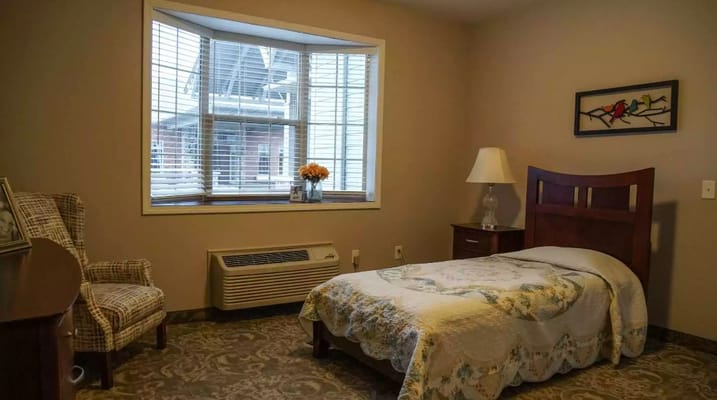 A cozy bedroom with a bed, chair, and window in Serene Gardens