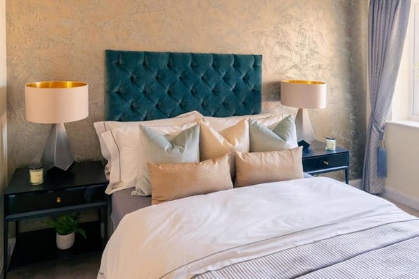 A stylish bedroom with a tufted teal headboard, decorative pillows, and bedside lamps.