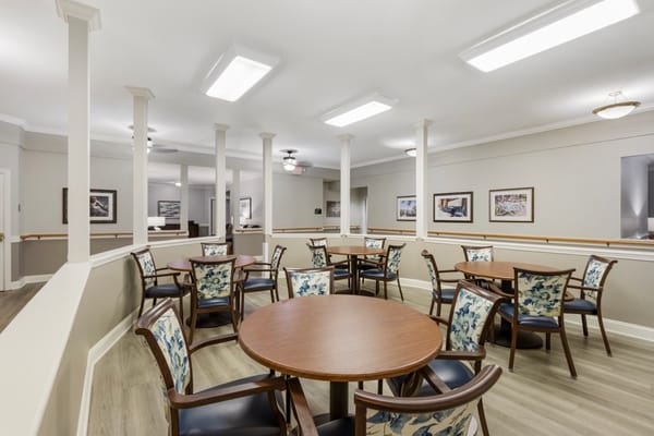 A dining area with round tables and floral chairs in a senior living facility.