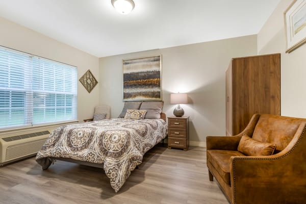 A cozy bedroom with a bed, chair, and lamp.