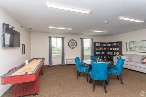 Cozy game room with a shuffleboard table, blue chairs, and bookshelves.