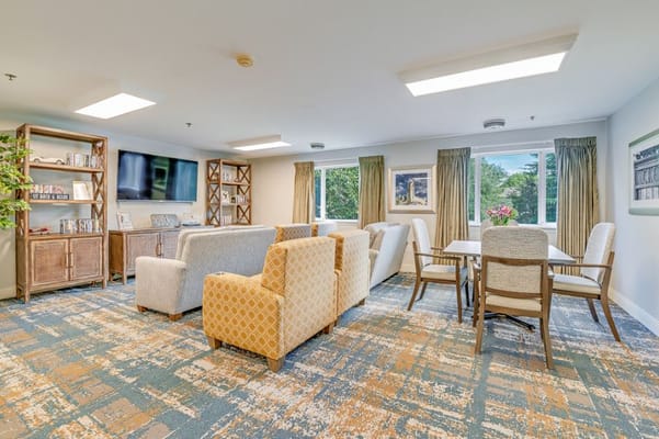 A cozy common area with comfortable seating and a dining table, large windows, and a TV.