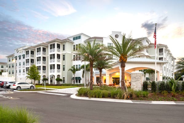 Entrance of Sonata Lake Mary senior living facility with palm trees and the American flag