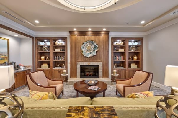 A cozy living area with comfortable seating, a fireplace, and shelves filled with decorative items.