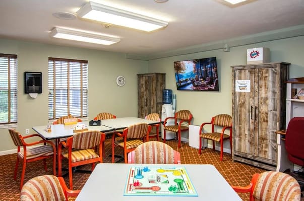 Bright common area with tables, chairs, and a TV.