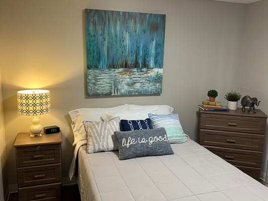 A well-decorated senior bedroom with a bed, artwork, and bedside tables.