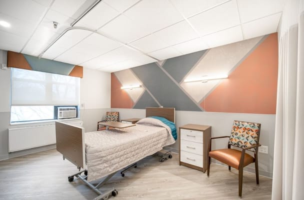 A well-furnished bedroom with a hospital bed, side table, and armchair.