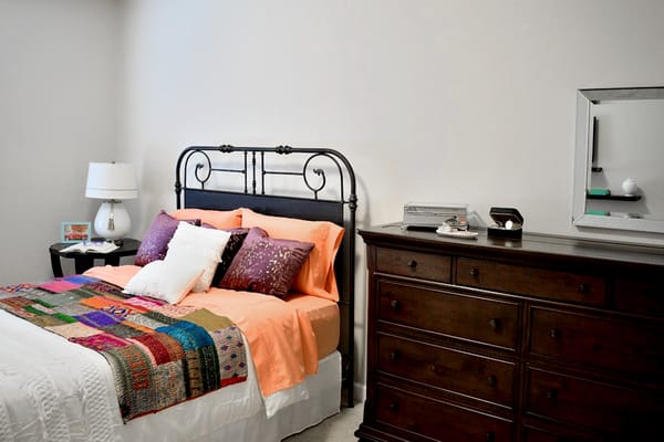 A cozy bedroom featuring a black iron bed frame, colorful bedding, and a wooden dresser.