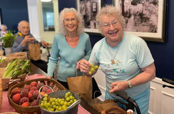 Two senior women smiling while selecting fresh produce.