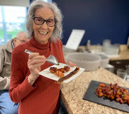 Senior resident smiling while holding a plate of food.